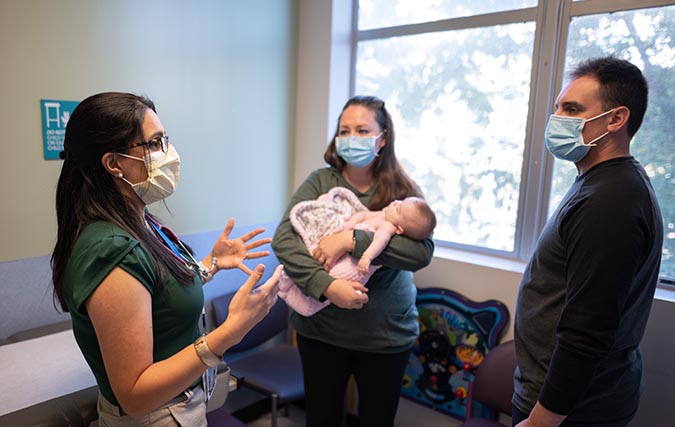 Physician meeting with parents while mother holds baby in her arms wrapped in pink blanket