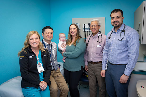 Three Cardiology physicians and one nurse with mother holding child in arms, all in exam room