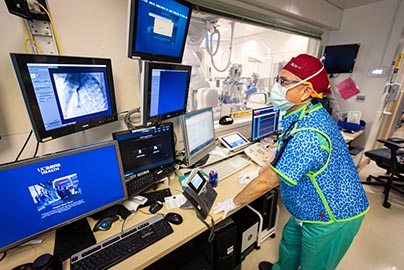 Physician in cath lab with full gear and scrubs using computer