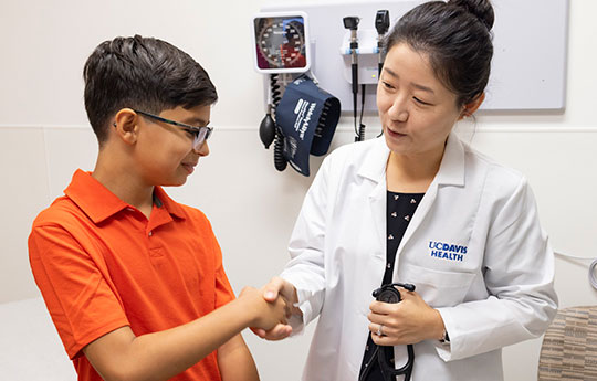 Physician shakes hands with young male patient in orange shirt