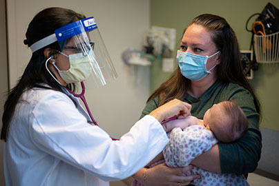Physicians in exam room with pediatric patient and mother, examining baby in mothers arms