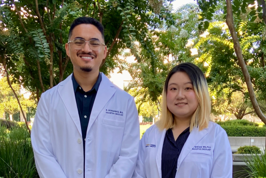 Two medical physics residents wearing white coats standing and smiling outdoors