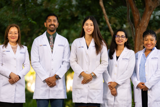 Radiation Oncology residents wearing their white coats standing upright and smiling outdoors