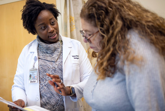 Two people having a discussion, sitting across from each other in a medical office, one holding papers.