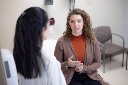 A healthcare consultation in an exam room, where one person speaks with another person seated across.